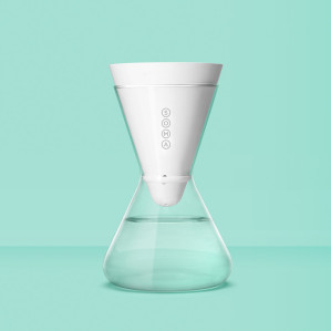 A modern, white water filter pitcher with a conical design, labeled "SOMA," set against a teal background.