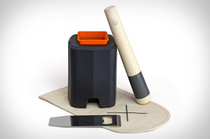 The image shows a sleek, modern cocktail smoking kit consisting of a black and orange smoking chamber, a wooden smoking stick, a metal plate, and a cloth mat.