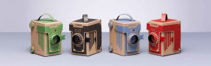 Cardboard pinhole cameras in green, black, blue, and red with decorative detailing and carrying handles, labeled "VIDDY."